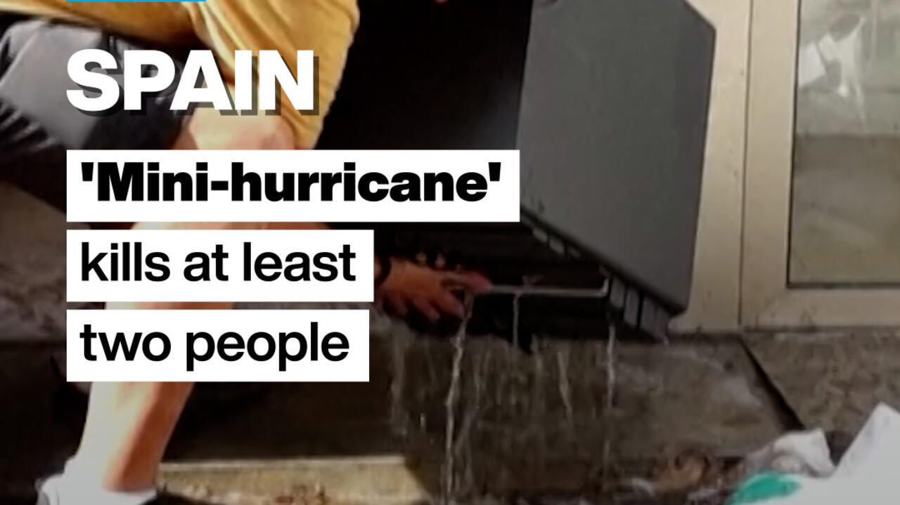 A person stands beside a washing machine as water spills across a flooded indoor floor.