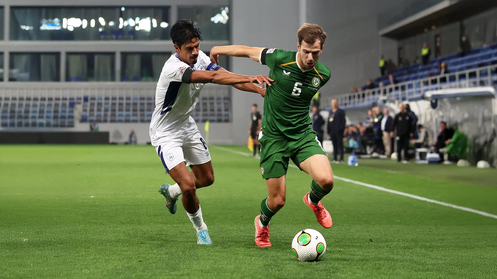 An Ireland player in green and an Israel player in white challenge for the ball during a match.