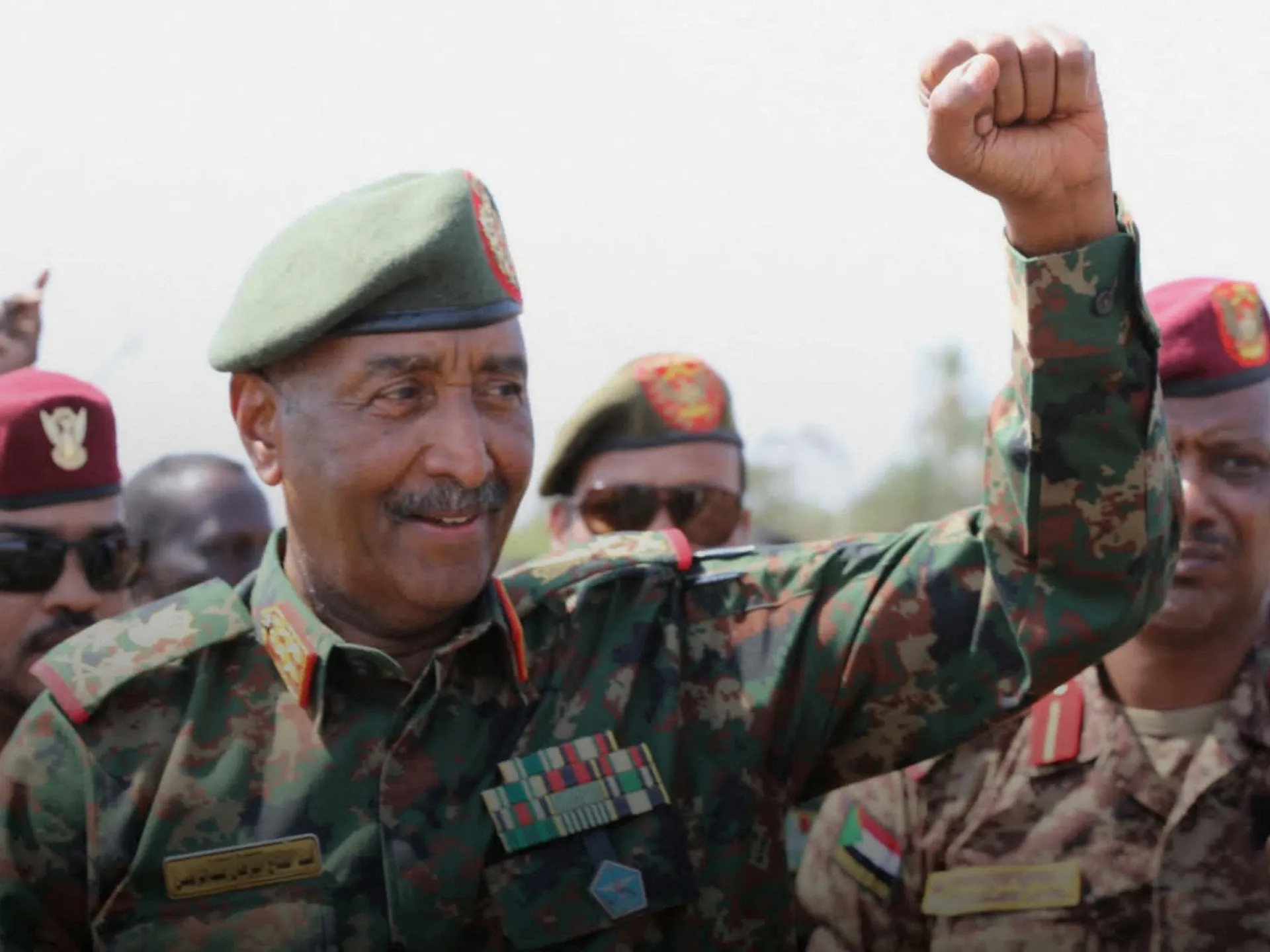 Uniformed officer raises a clenched fist among soldiers wearing camouflage uniforms and berets.