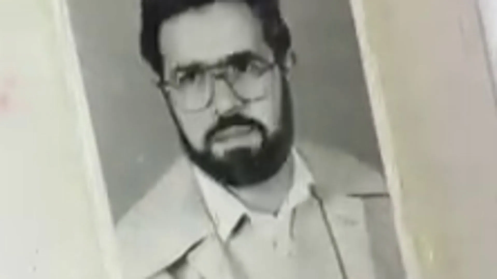 A black-and-white portrait of a bearded man wearing glasses and a light-colored suit.