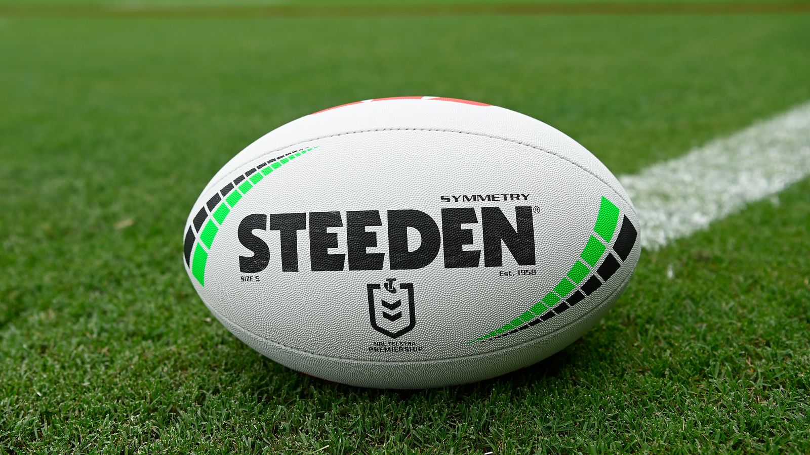 A white Steeden rugby league ball rests on grass beside a painted field line.