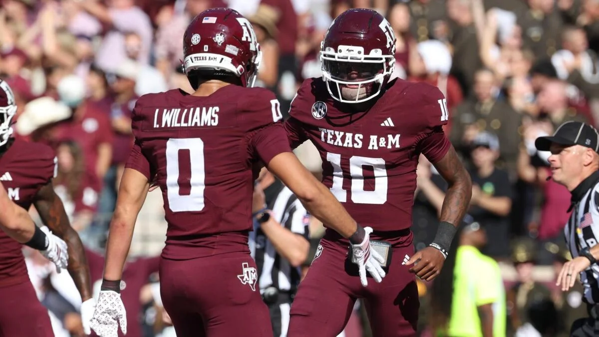 Texas A&M players in maroon uniforms meet on the field during a game.