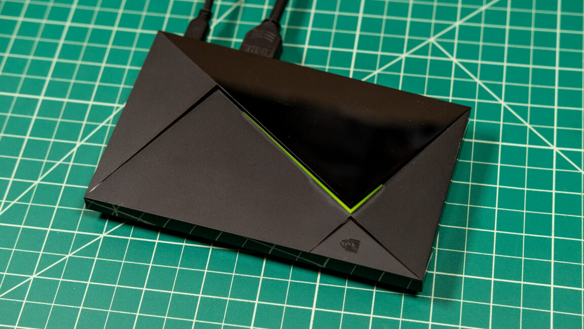 Black Nvidia Shield TV device with cables rests on a green gridded cutting mat.