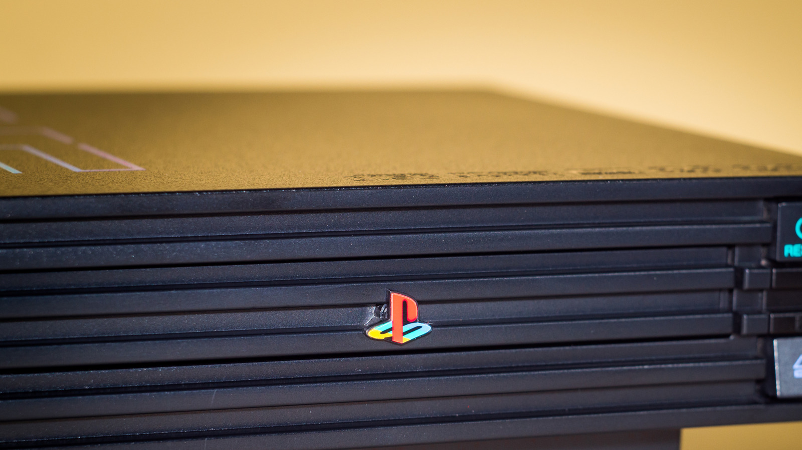 Close-up of a black PlayStation 2 console with a multicolored PlayStation logo against a warm background.
