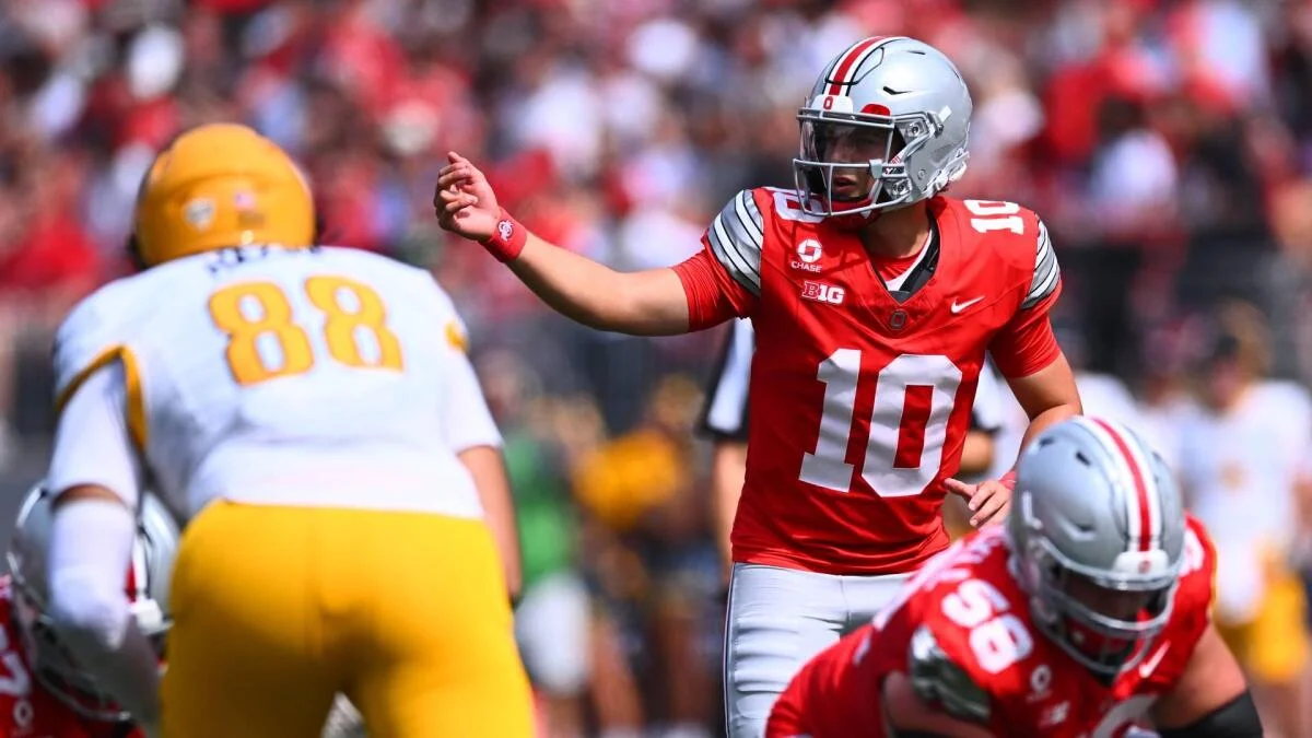 Ohio State player in a red number 10 jersey signals across the field during a football game.