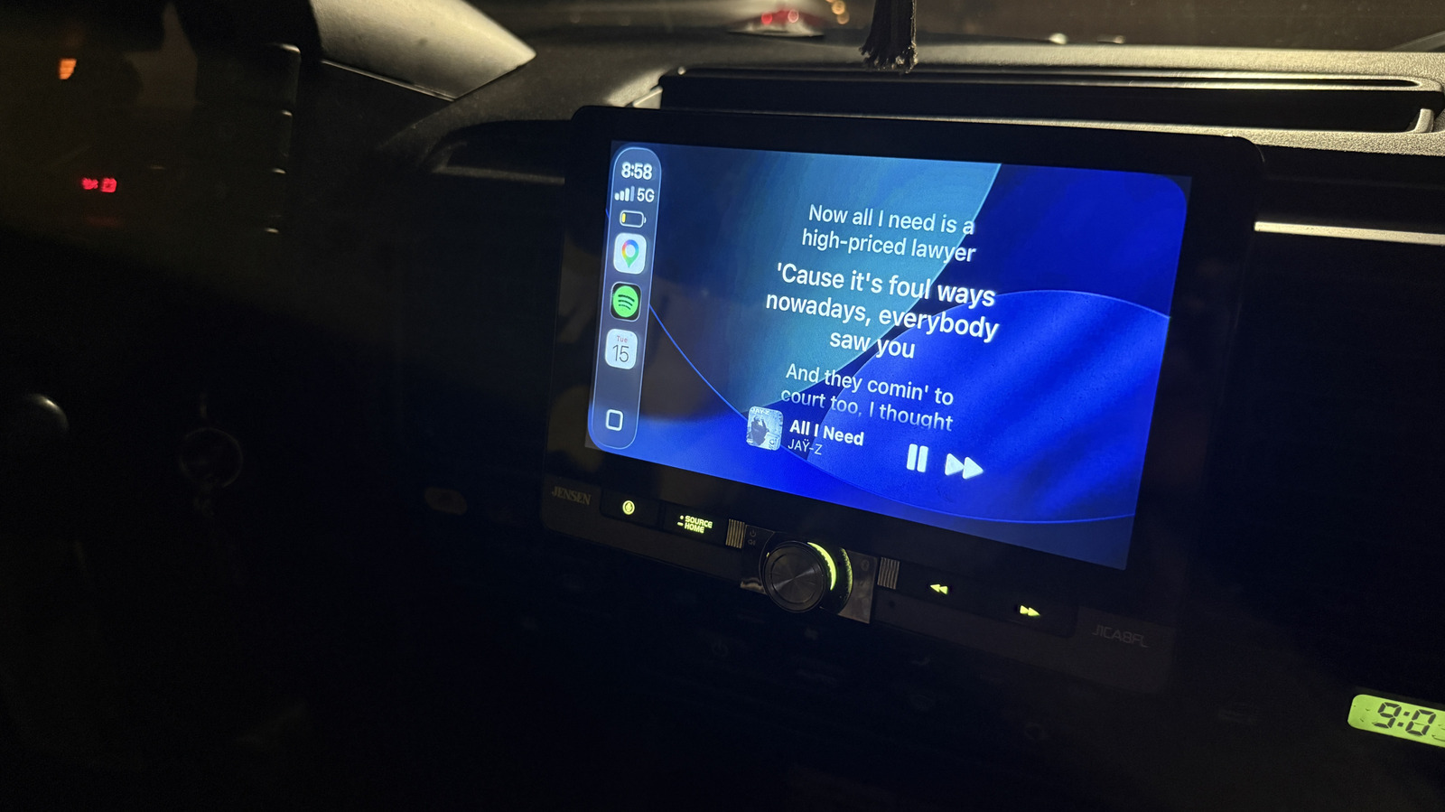 Car infotainment screen displays song lyrics and playback controls in a dark vehicle.
