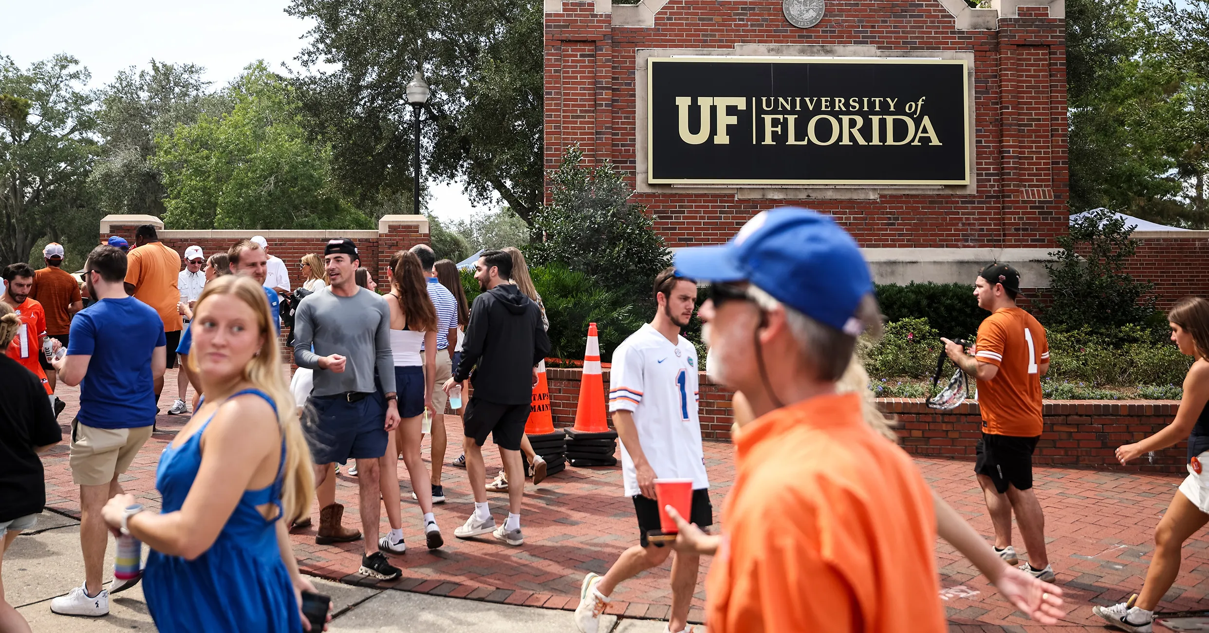 Crowd in orange and blue gathers outside a brick entrance bearing a University of Florida sign.