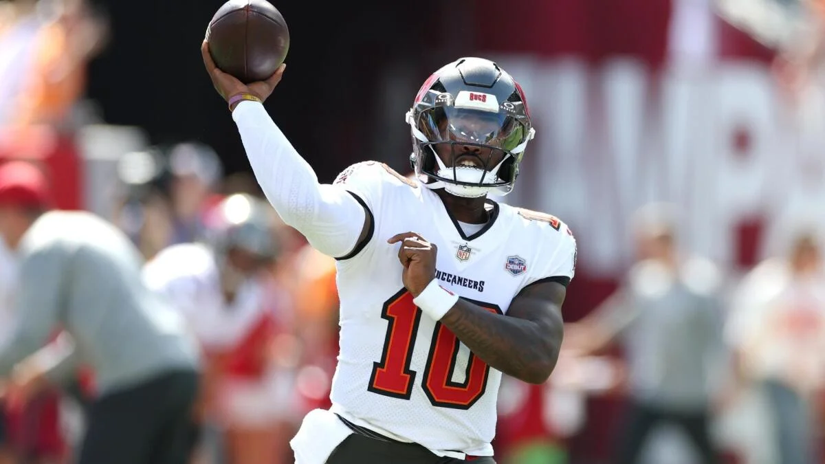 Buccaneers quarterback in a white number 10 jersey raises a football to throw.