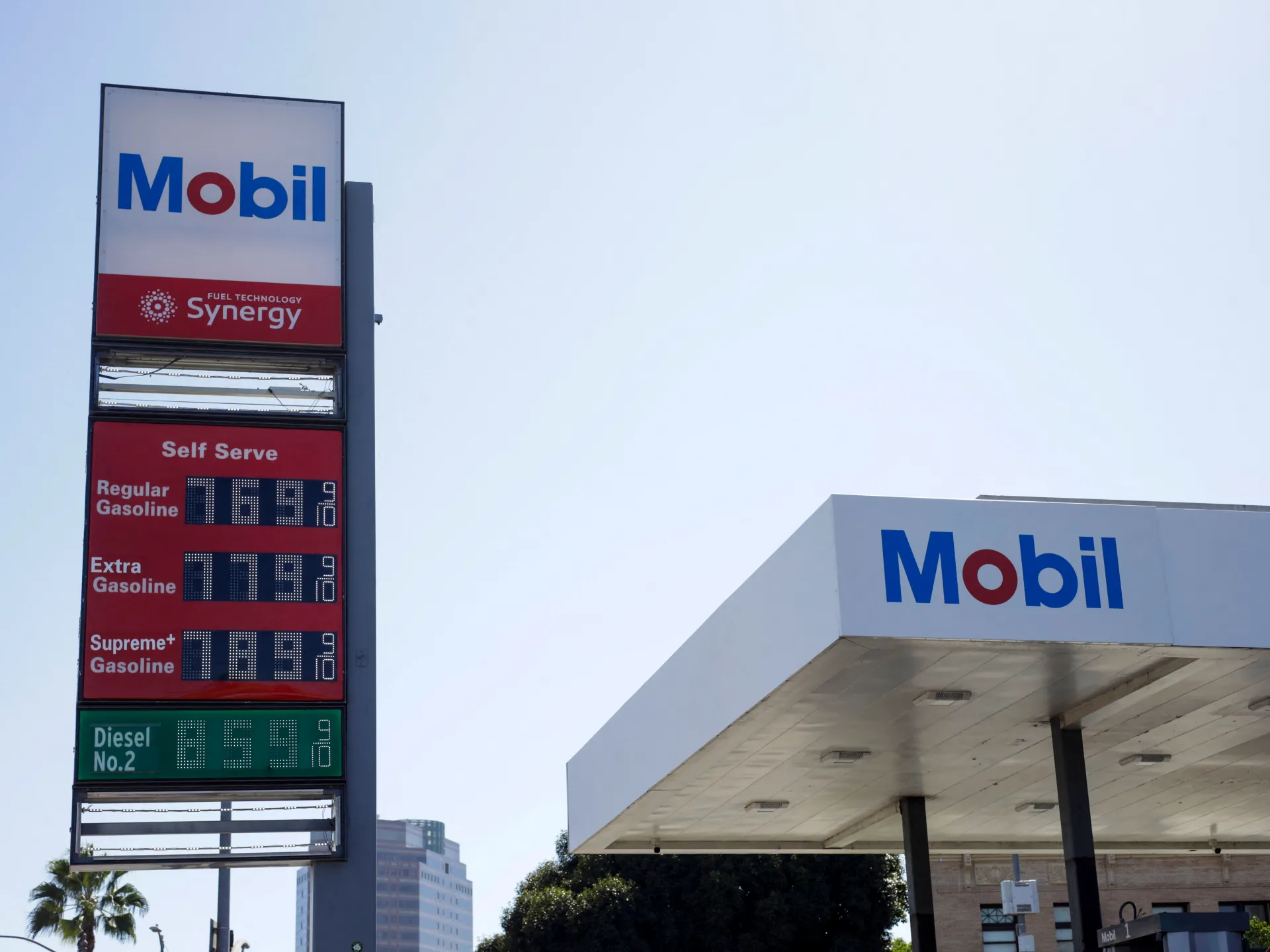 A Mobil gas station canopy and roadside price sign display gasoline and diesel prices beneath a clear sky.