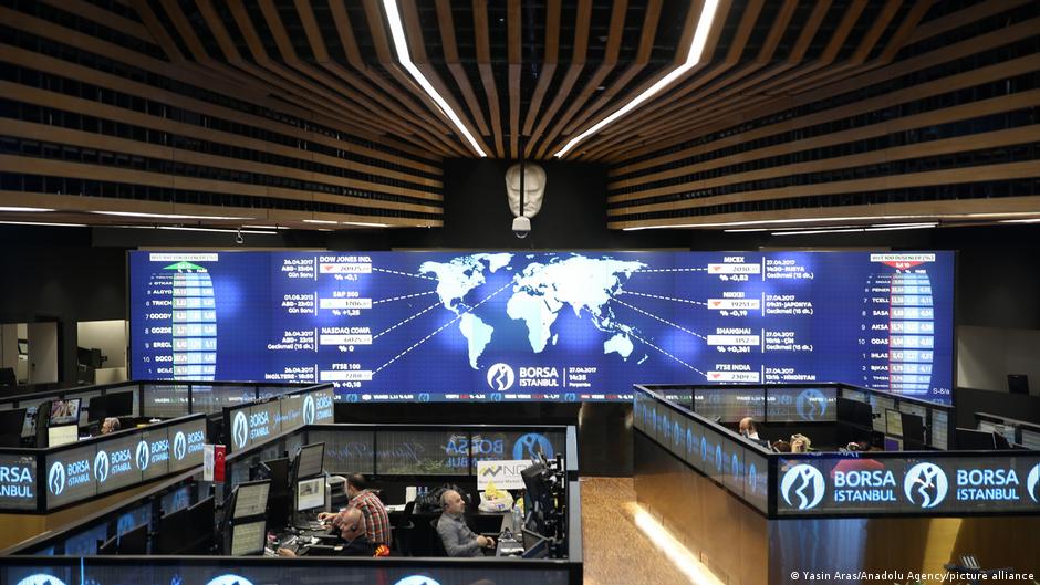 A wide electronic market board displays financial data above trading desks in a modern exchange hall.