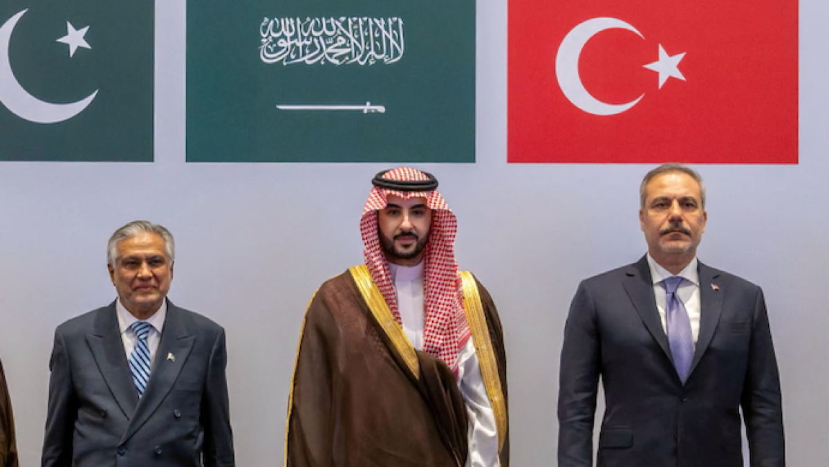 Three men stand beneath Pakistan, Saudi Arabia, and Türkiye flags at an official gathering.