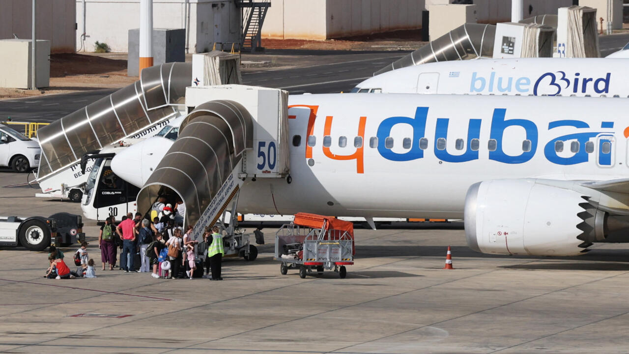 Passengers board a Flydubai aircraft using mobile stairs as airport staff and ground vehicles stand nearby.