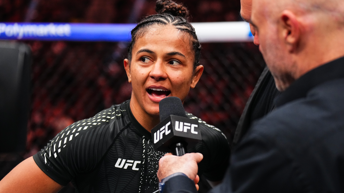 A female UFC fighter speaks into a microphone held by an interviewer inside the octagon.