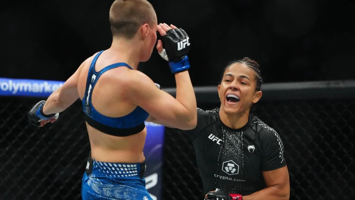 Two UFC fighters face each other in the octagon, one raising a gloved hand as the other smiles.