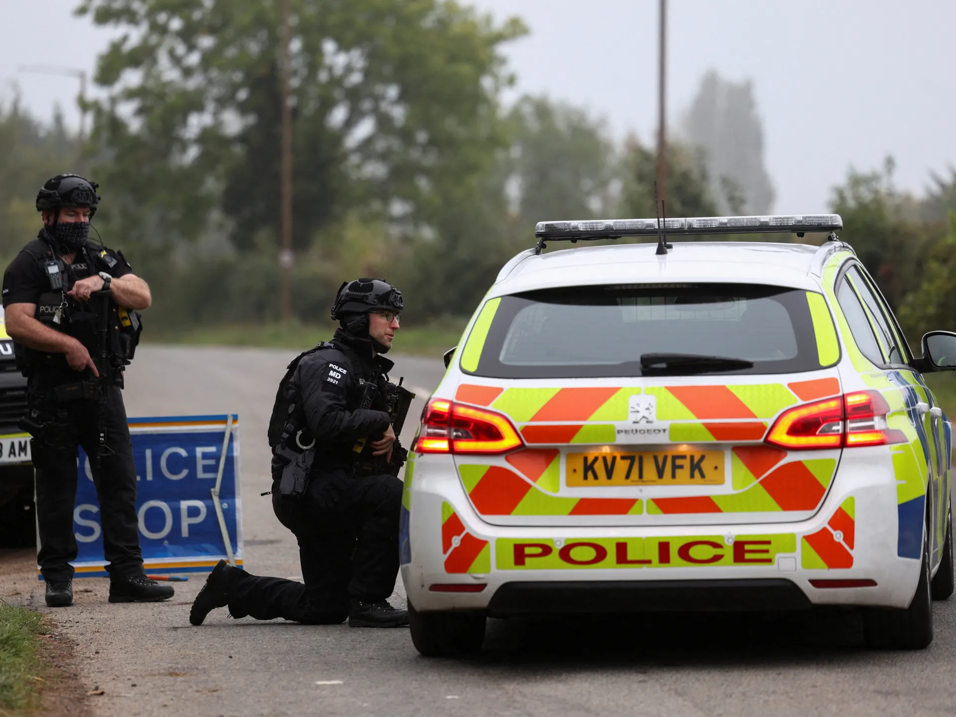 Armed police officers beside a marked police car at a roadside cordon.