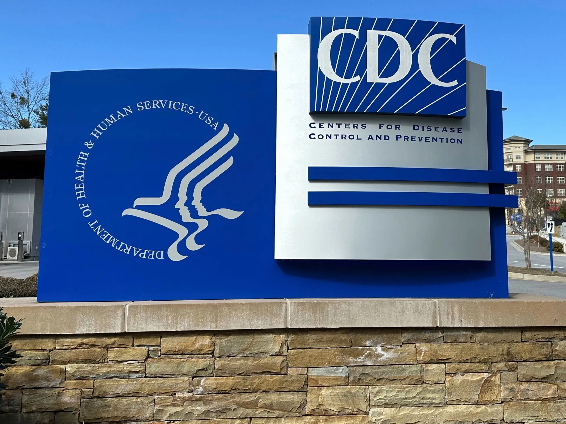 Blue CDC and Department of Health and Human Services sign outside a building under a clear sky.