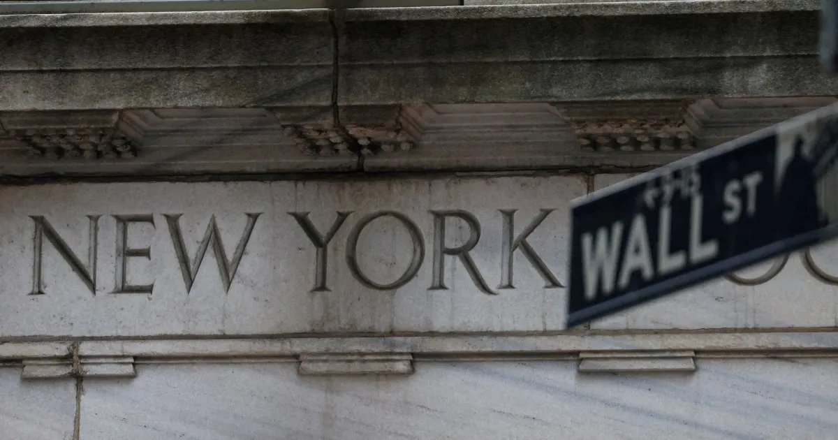 Carved stone facade reading New York, partly obscured by a blurred Wall Street street sign.