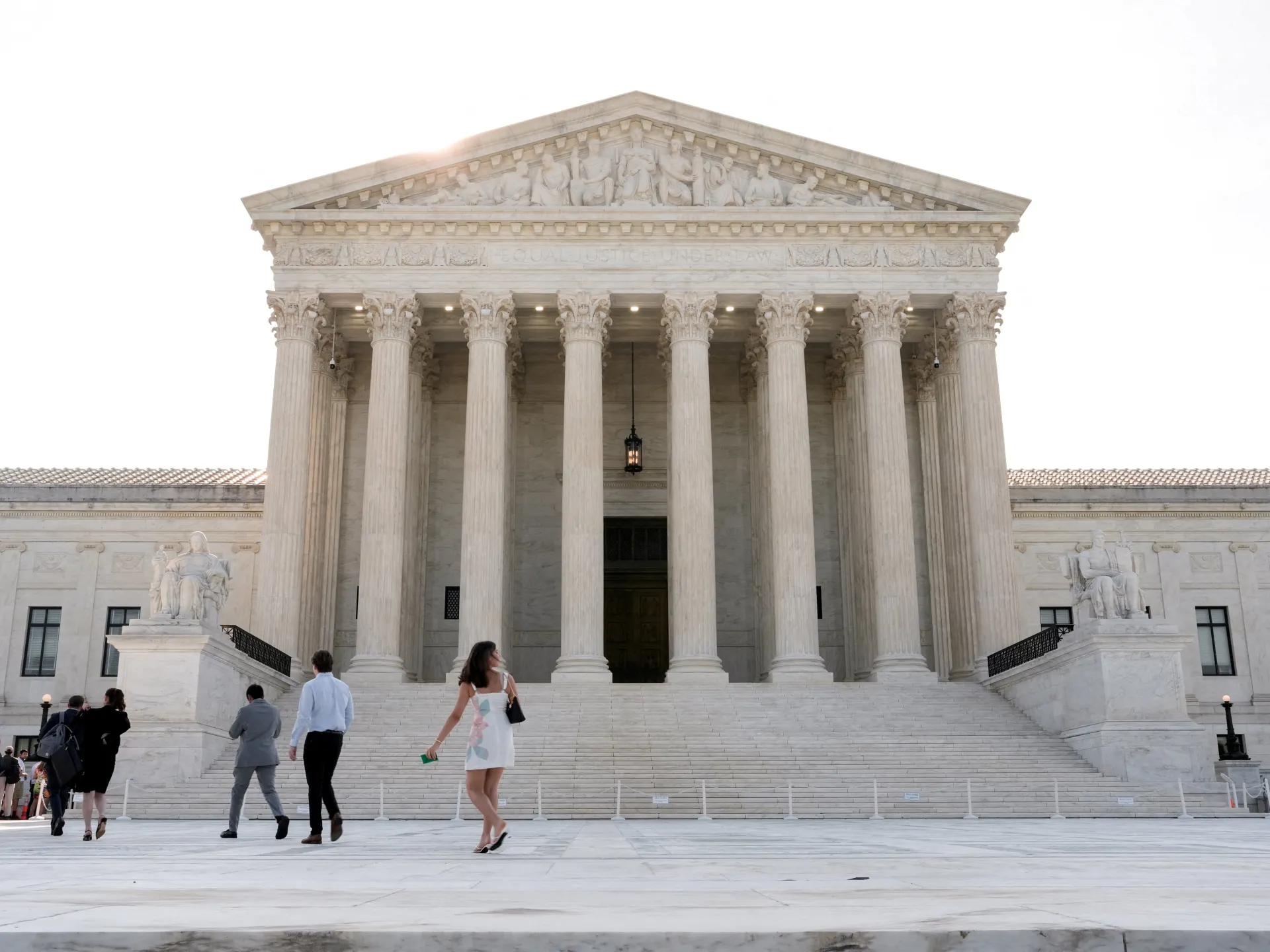 Visitors walk across the plaza in front of a large neoclassical building with tall columns and broad steps.