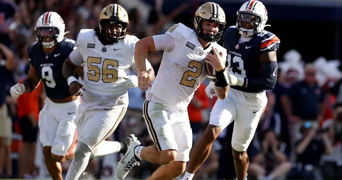 A Vanderbilt quarterback runs with the ball as Auburn defenders pursue during a football game.