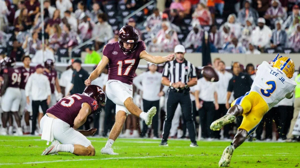 Virginia Tech kicker in maroon attempts a field goal as a Pitt player in yellow rushes toward him.