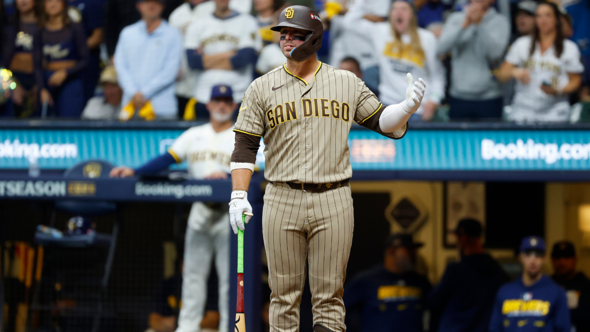 Padres batter in a tan pinstriped uniform gestures while holding a bat during a game.