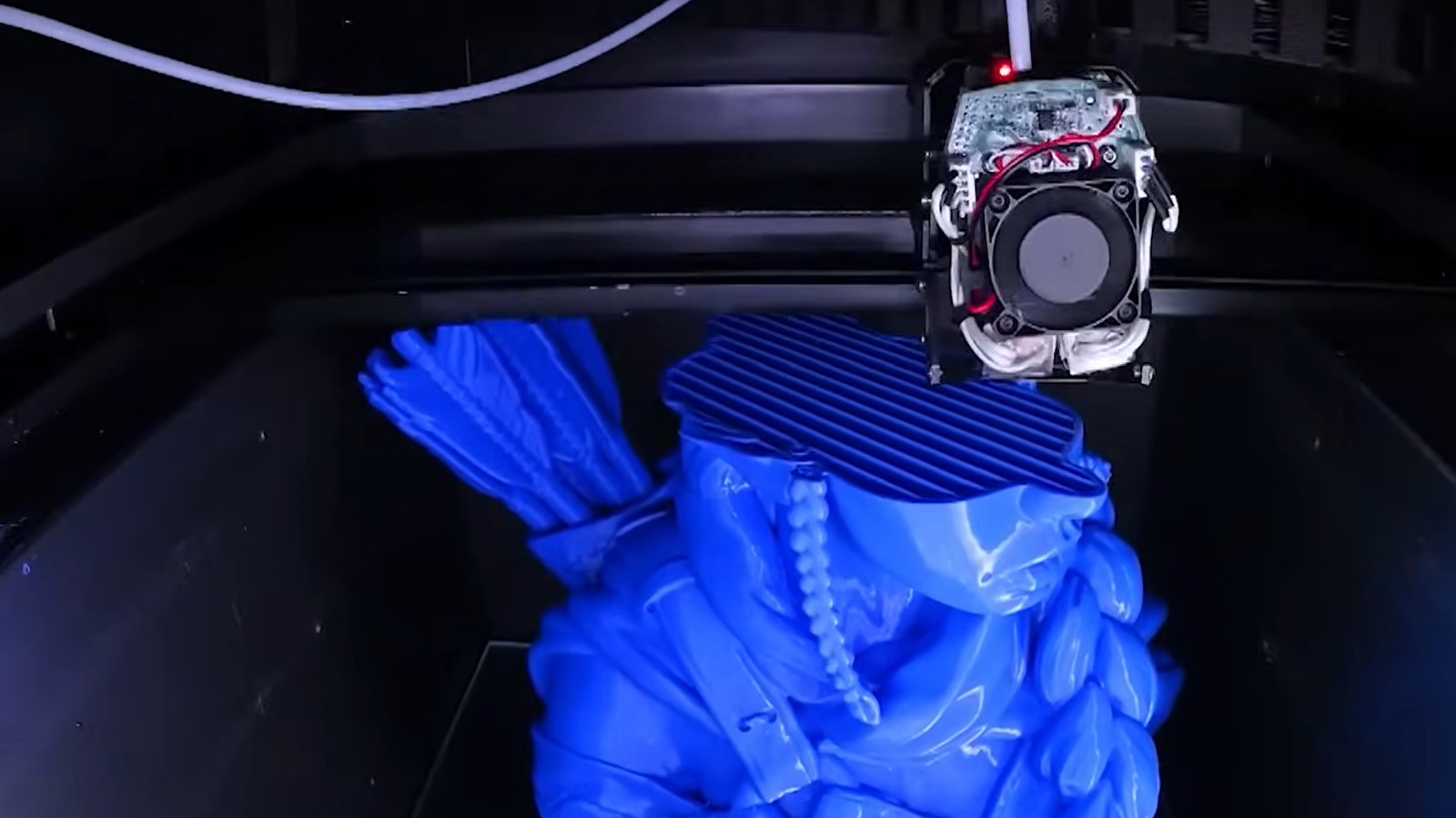 A 3D printer nozzle deposits blue filament onto a partially formed object inside the printer.