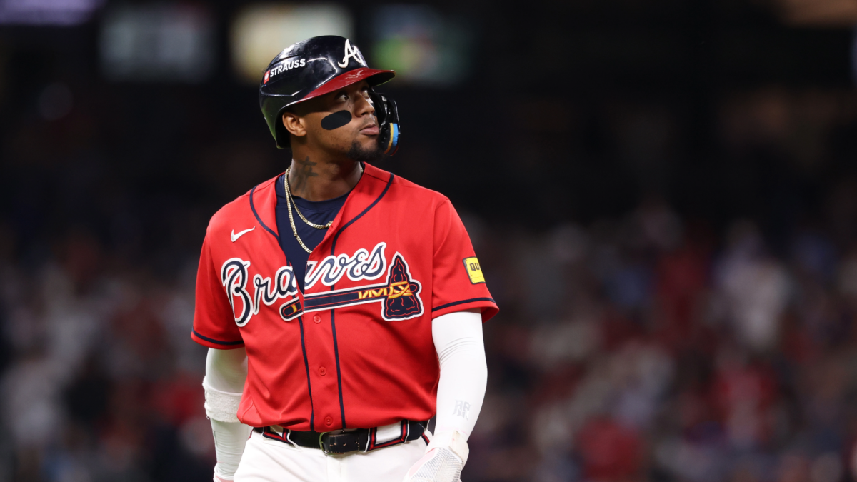 A Braves player in a red jersey and black helmet looks upward during a game.