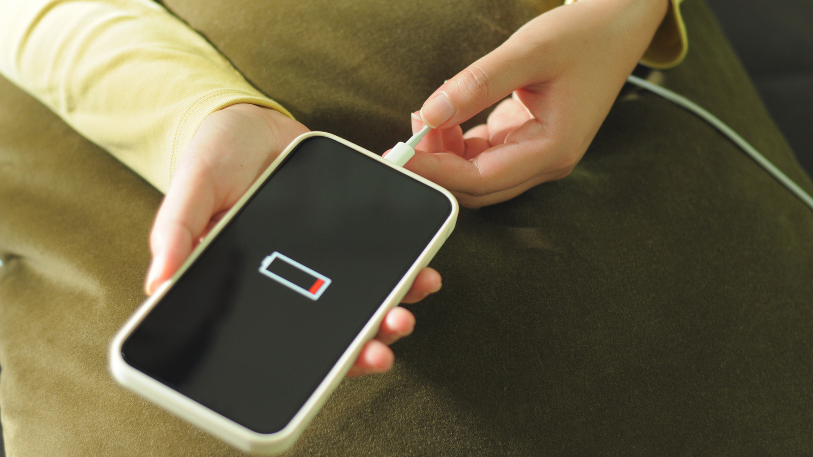 A person connects a charging cable to a smartphone showing a nearly empty battery icon.