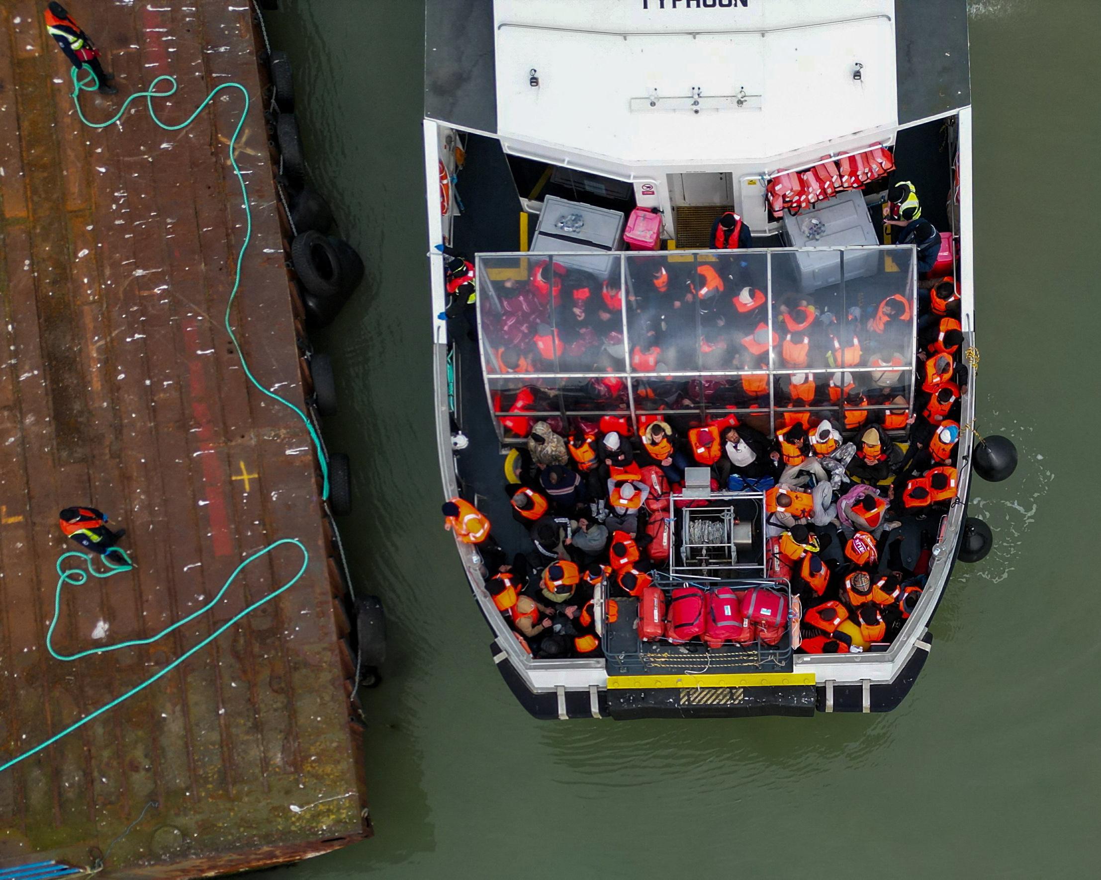 Overhead view of a crowded boat carrying people in orange life jackets beside a larger vessel.