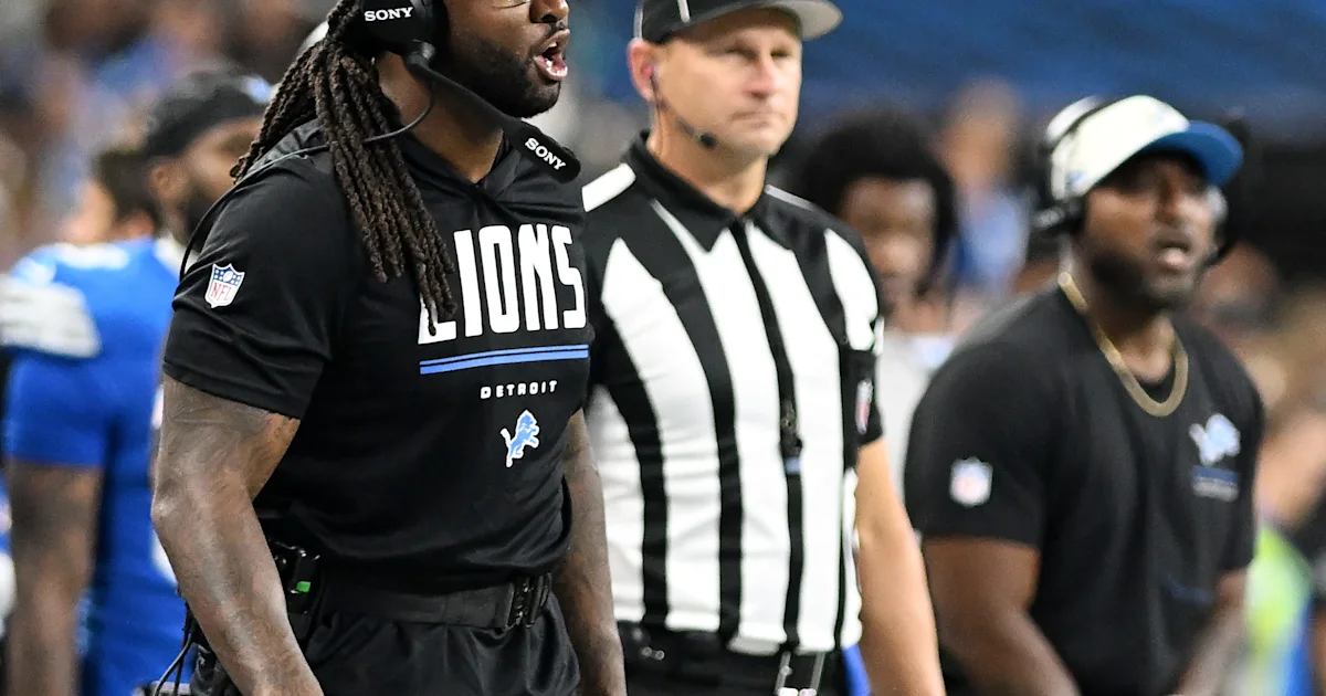 A Lions player wearing a headset stands beside a referee and another team staff member on the sideline.