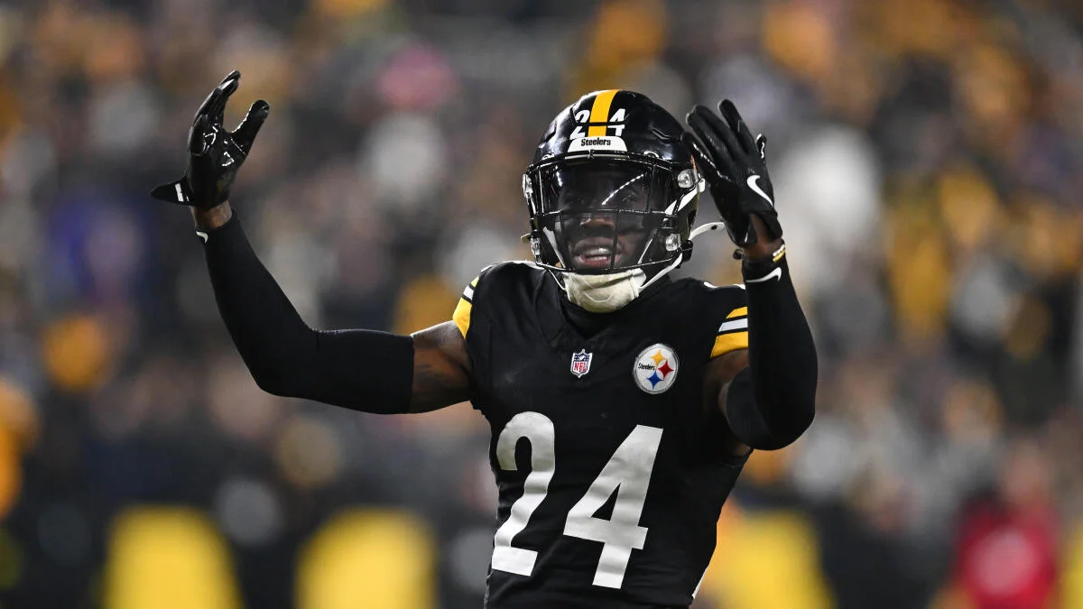 Football player in a black Steelers uniform, number 24, raises both hands during a game.