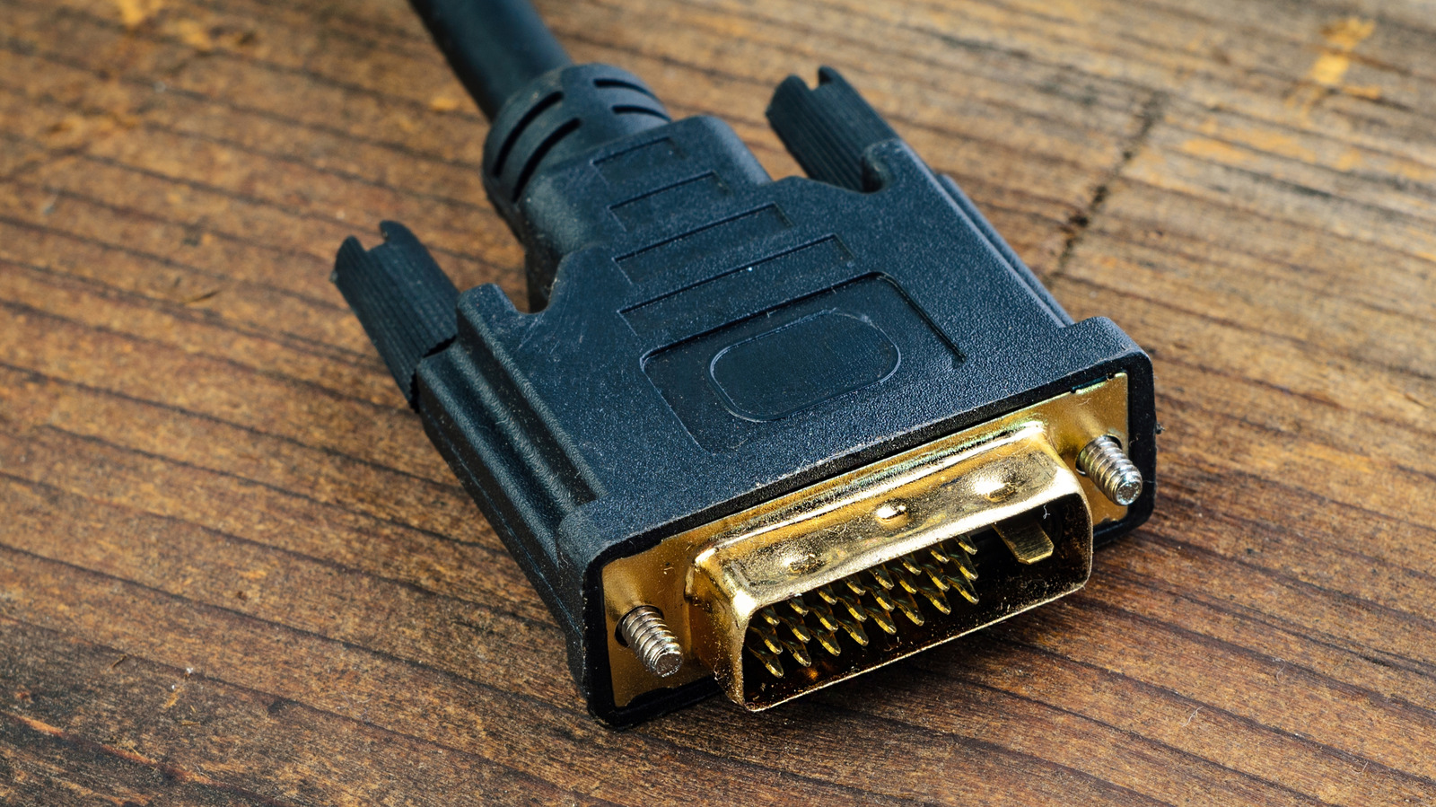 Close-up of a black video cable connector with gold-colored pins resting on a wooden surface.