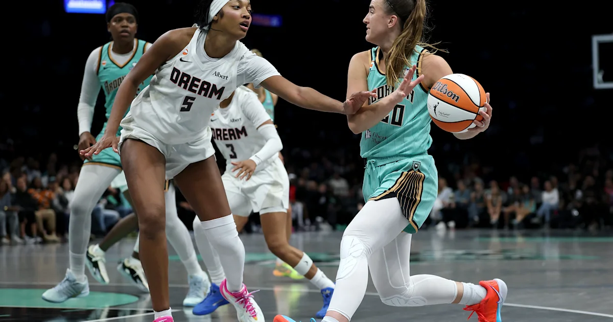 A teal-uniformed player holds the ball as a white-uniformed defender reaches toward her.