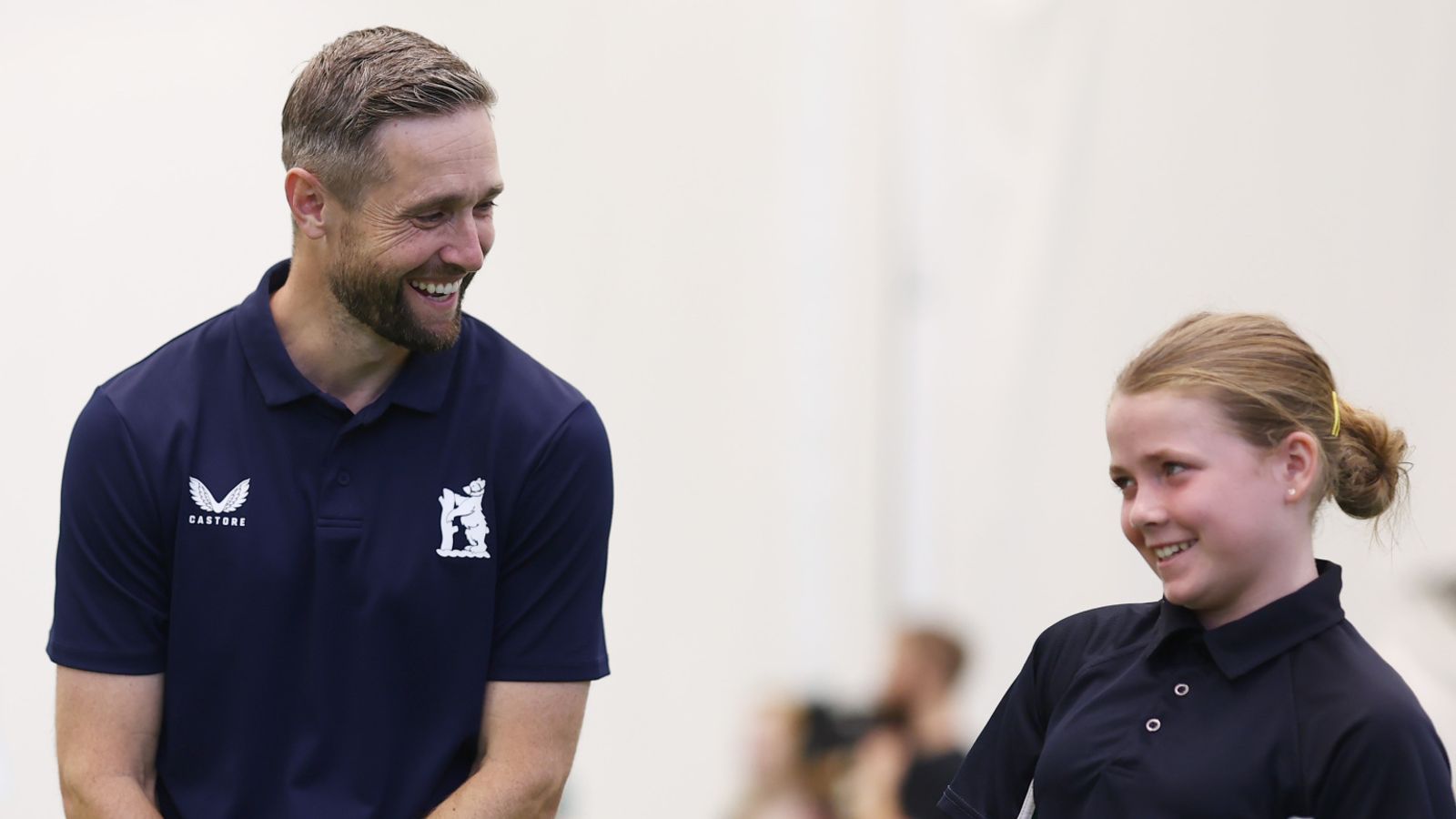 Smiling man in a navy polo chats with a smiling schoolgirl in a matching shirt.