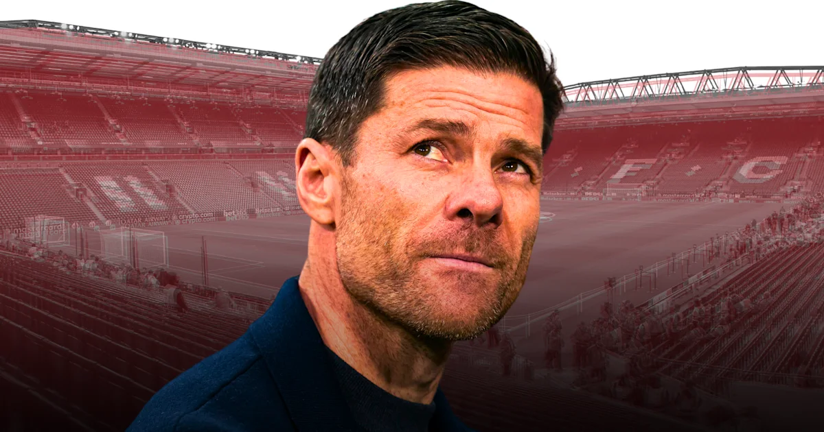 A man in a dark jacket looks upward in front of a red-tinted football stadium.
