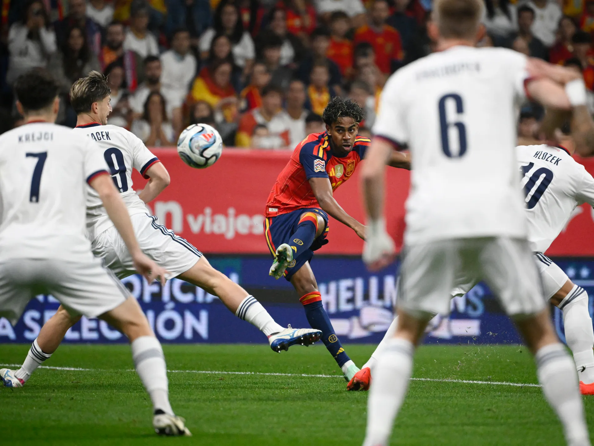 Spain player strikes the ball as Czechia players in white close in during a match.