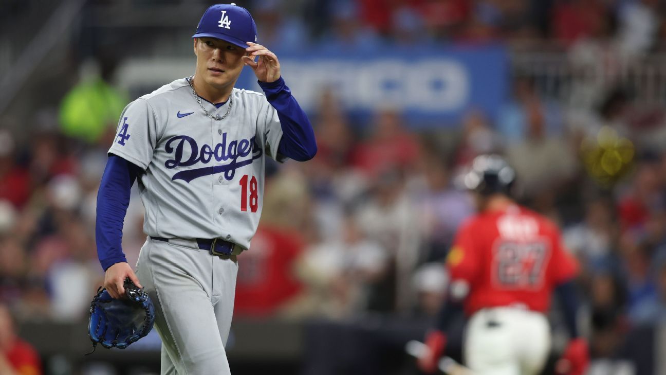 Dodgers pitcher in a gray uniform adjusts his cap while holding a glove on the field.