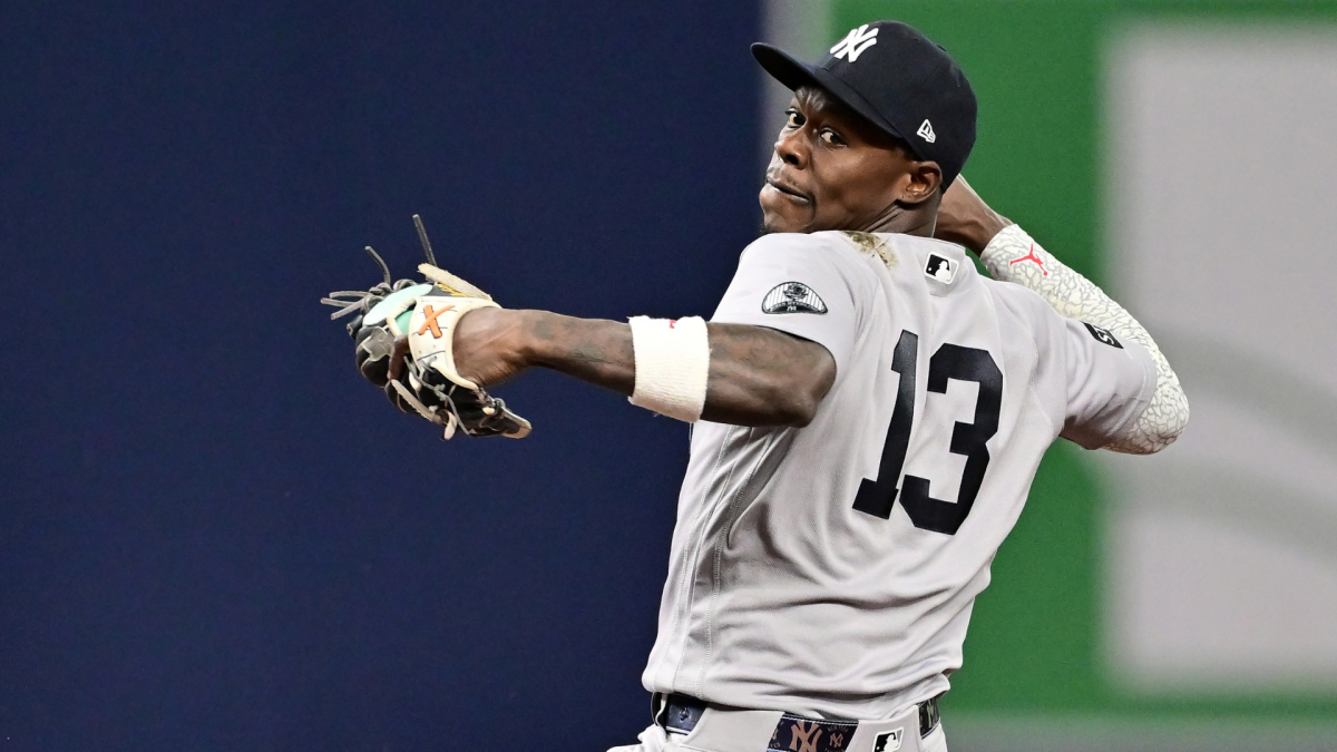 Yankees pitcher in gray number 13 uniform throws a baseball against a stadium backdrop.
