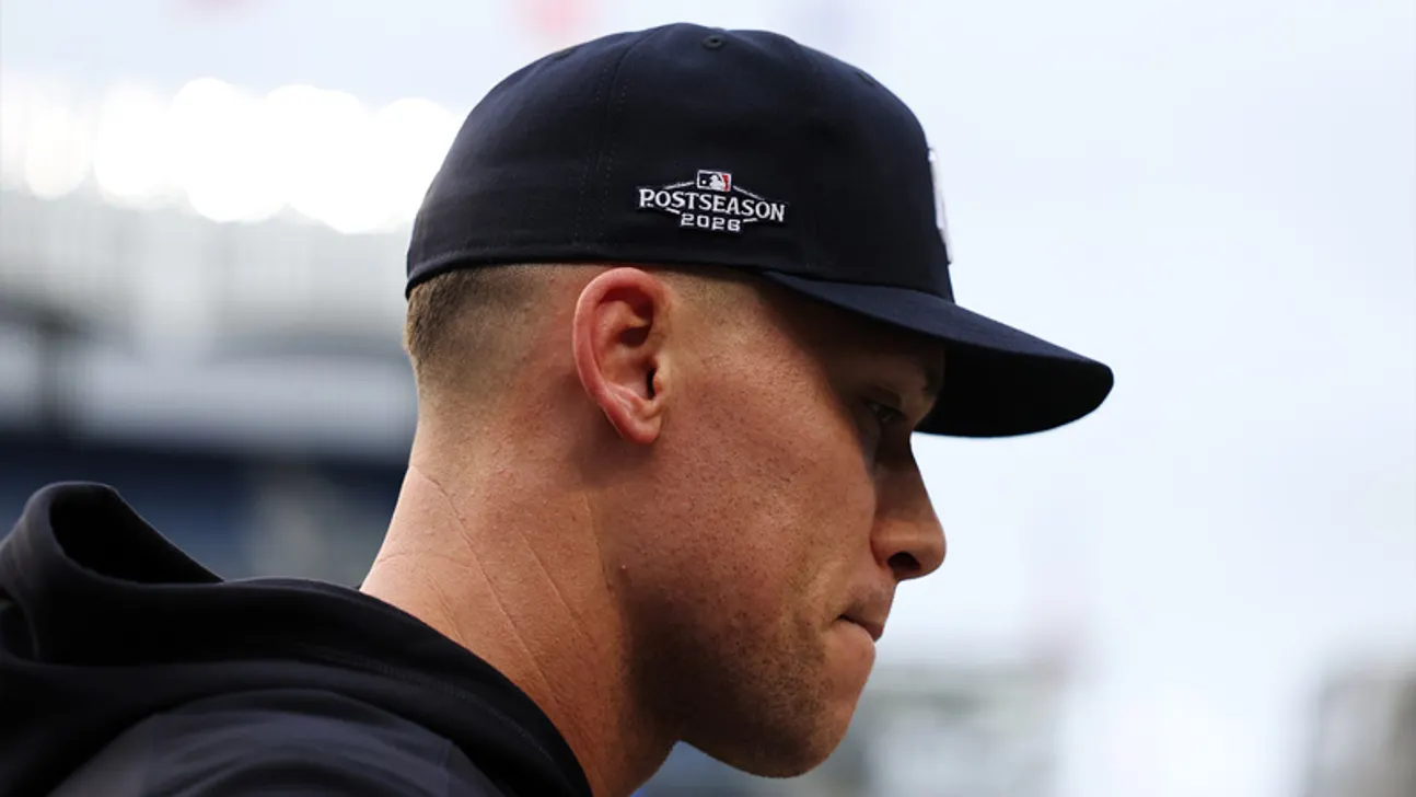 A man in profile wears a black postseason 2026 cap and dark hoodie.