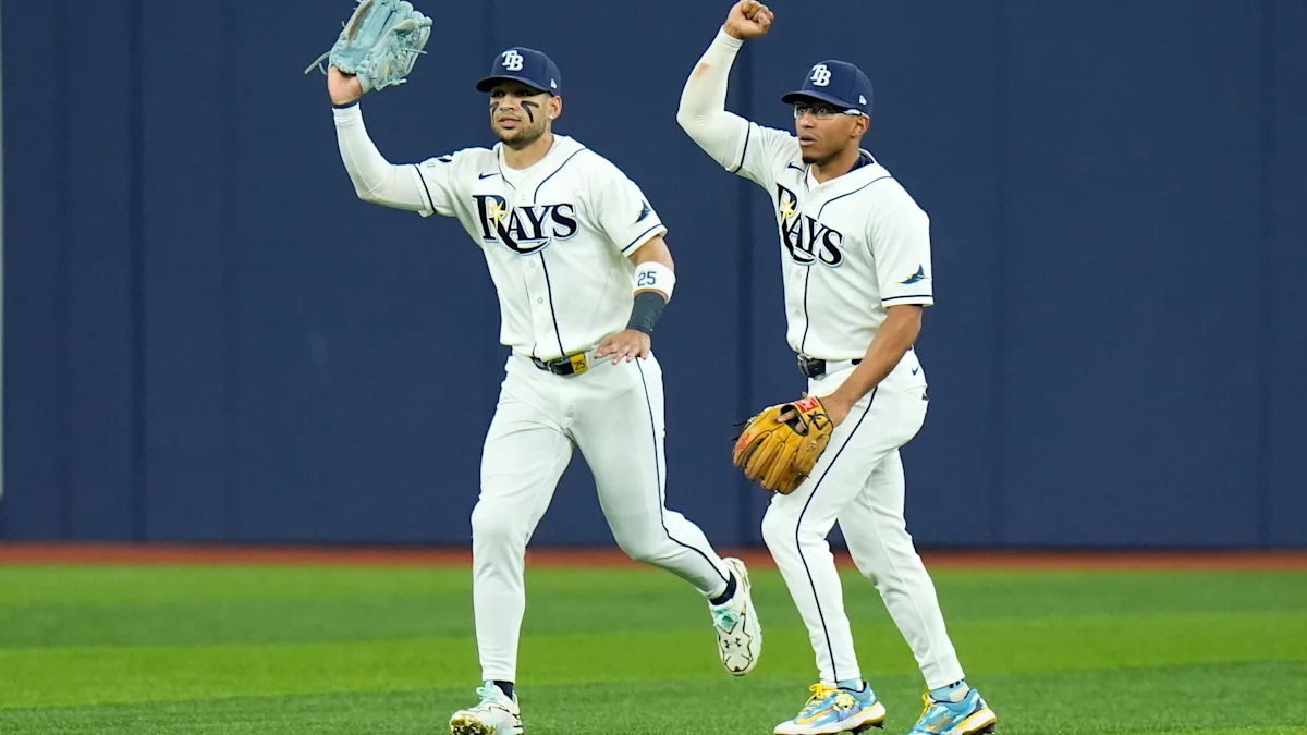 Two Tampa Bay Rays fielders stand on the grass, one raising his glove and the other a fist.