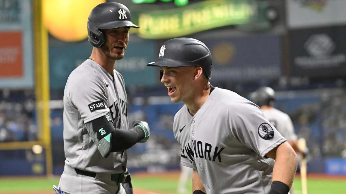 Two Yankees players in gray uniforms and batting helmets celebrate on the field during a game.