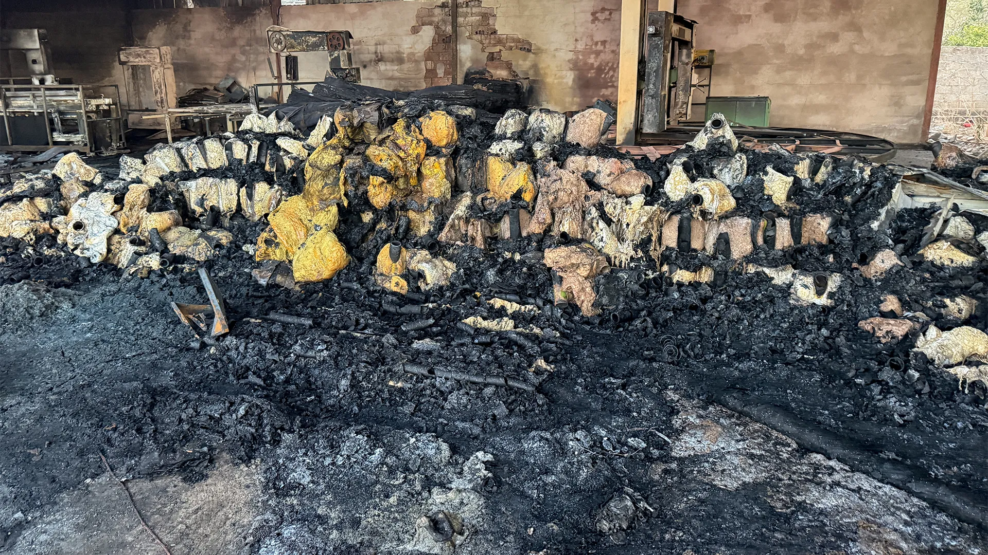 A fire-damaged workshop with charred debris and rows of scorched machinery parts across the floor.