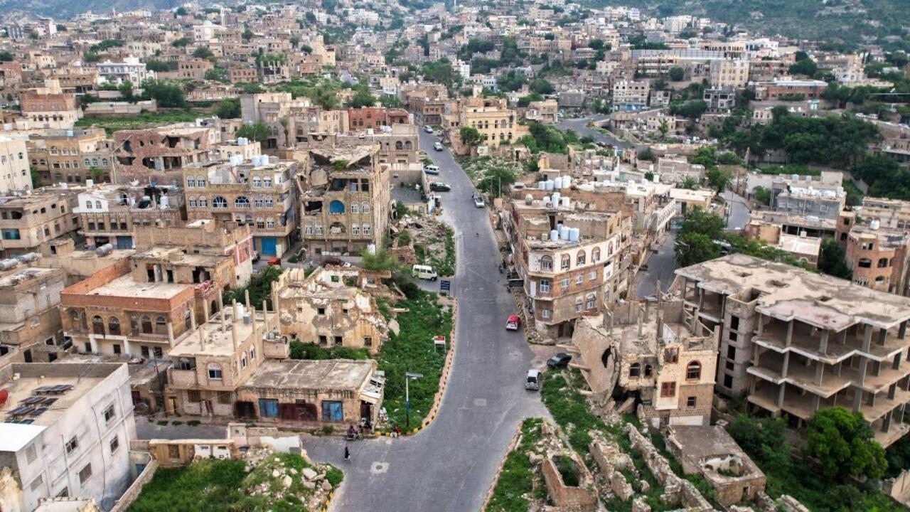 A winding road passes through a densely built hillside city, with damaged buildings and scattered rubble.