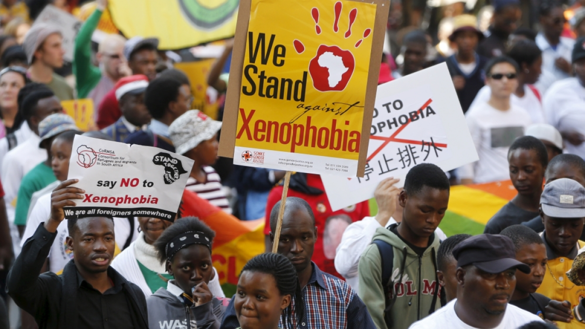 Crowd at a march holds signs opposing xenophobia, including one reading “We Stand against Xenophobia.”